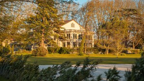 A large, historic building with multiple windows and a prominent balcony, surrounded by lush greenery and trees. - Manoir le Roure (Chateauneuf-du-Rhone)