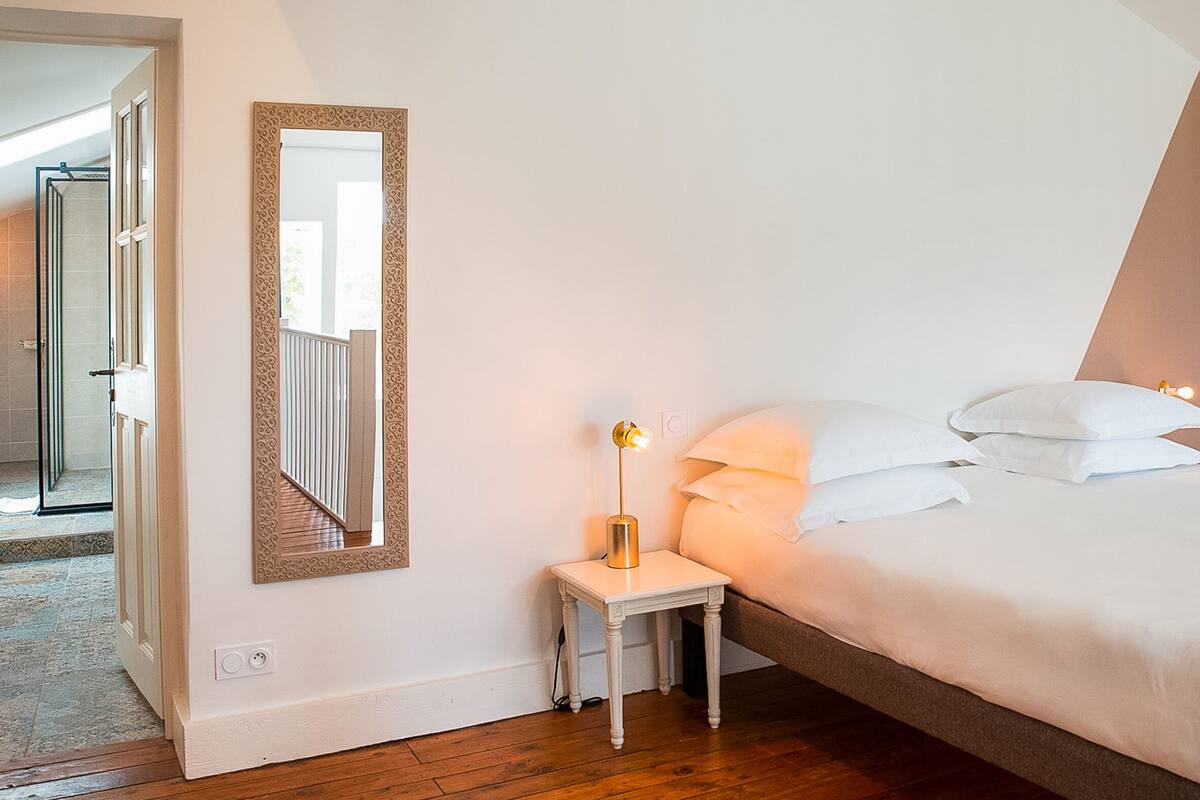 A bedroom with a bed, bedside table, lamp, and a mirror.