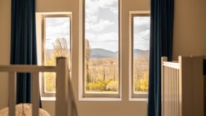 A room with three windows, a white radiator, and a view of a mountainous landscape. - Manoir le Roure (Chateauneuf-du-Rhone)