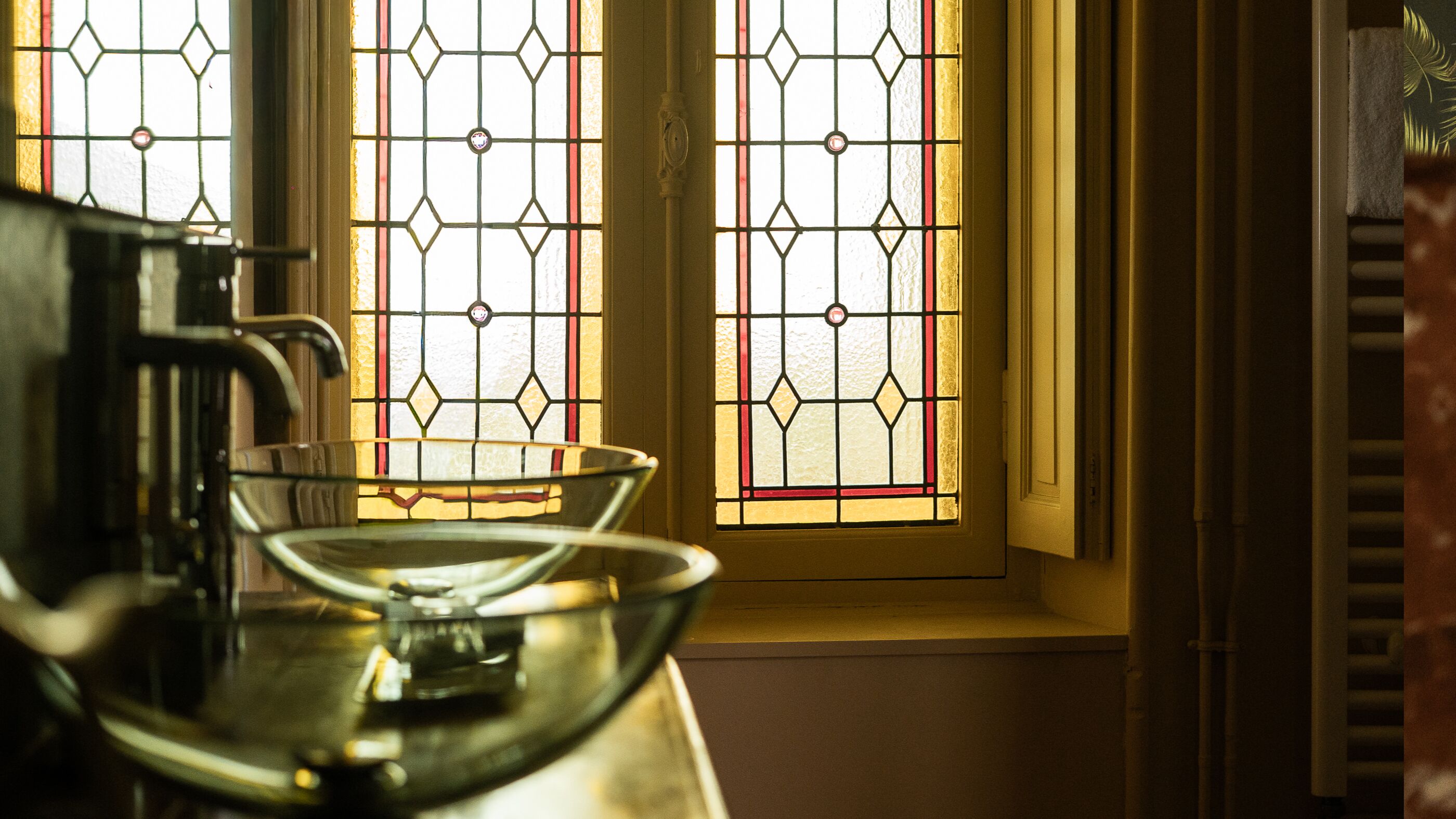 A kitchen area with a coffee maker, a glass bowl, and a window with stained glass.