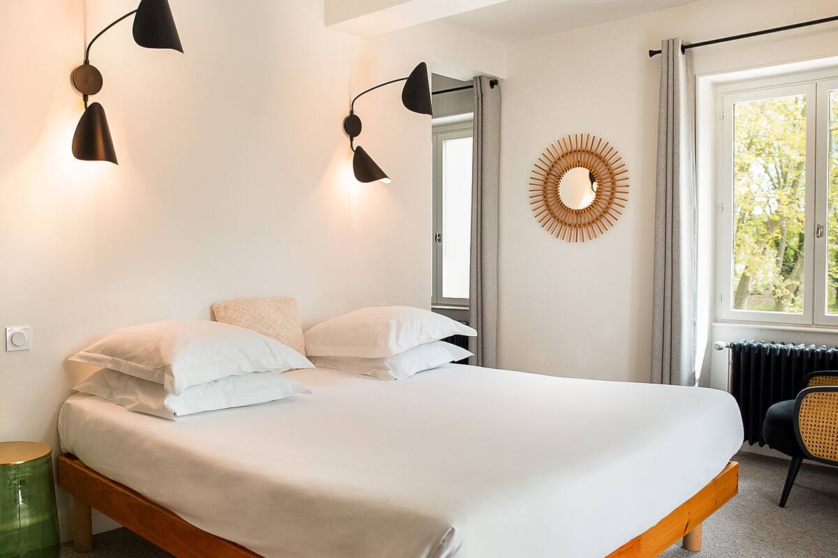 A bedroom with a bed, two wall-mounted lamps, a mirror, a window with curtains, and a radiator.