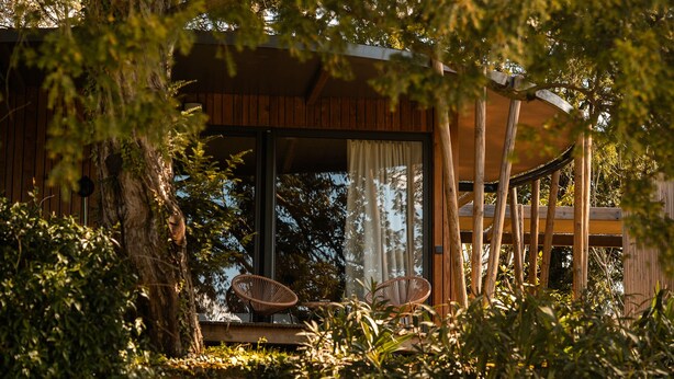 A wooden cabin with a covered porch, two wicker chairs, and a large window. - Manoir le Roure (Chateauneuf-du-Rhone)
