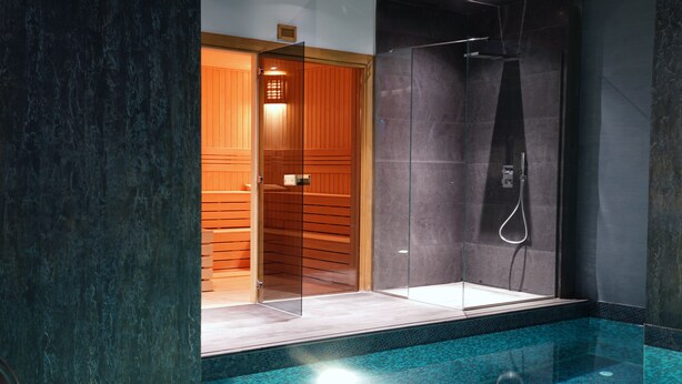 Een moderne badkamer met een douchecabine van glas, een houten deur naar een sauna, en een betegeld zwembadgedeelte.