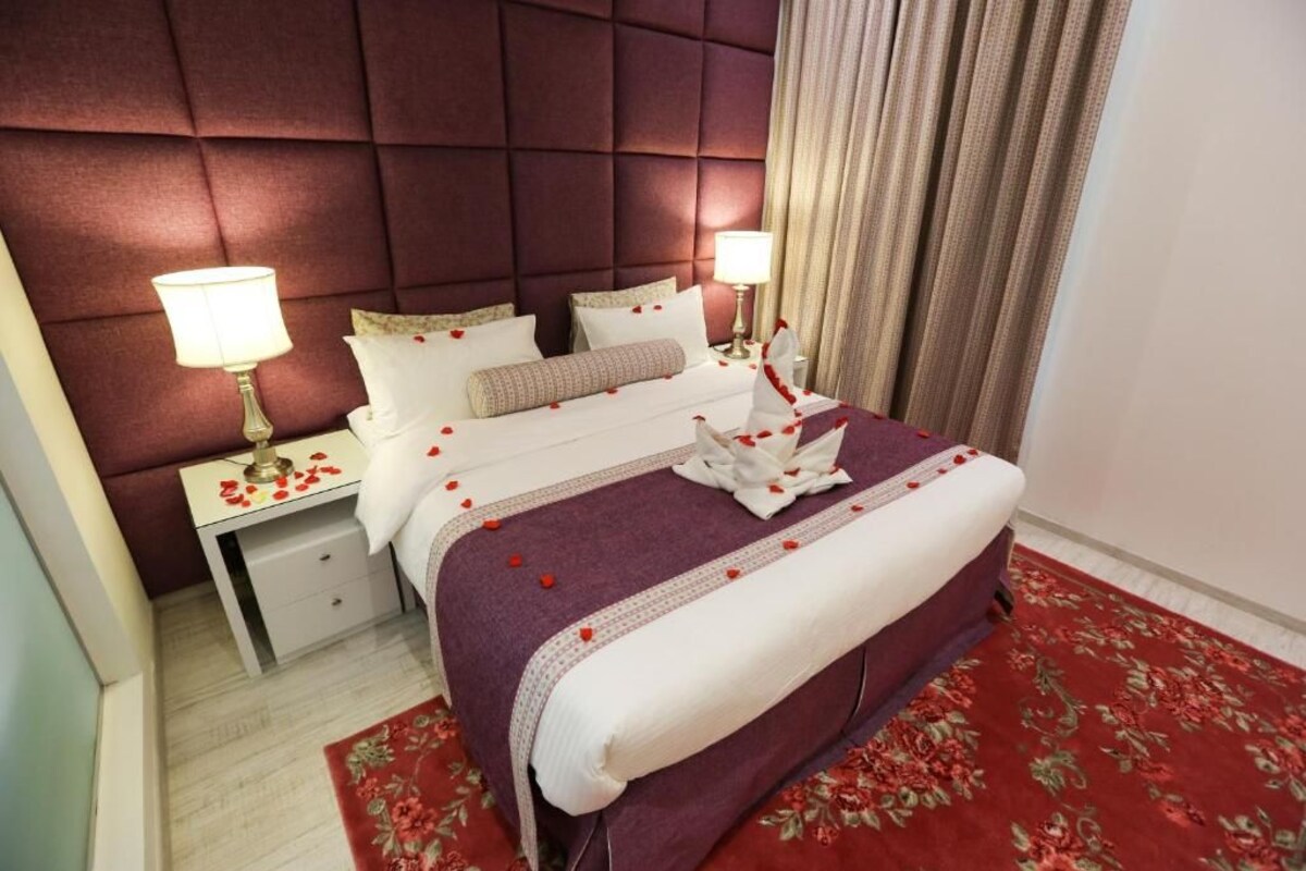 Une chambre d’hôtel avec un grand lit, deux tables de chevet et un tapis à motifs floraux rouges.