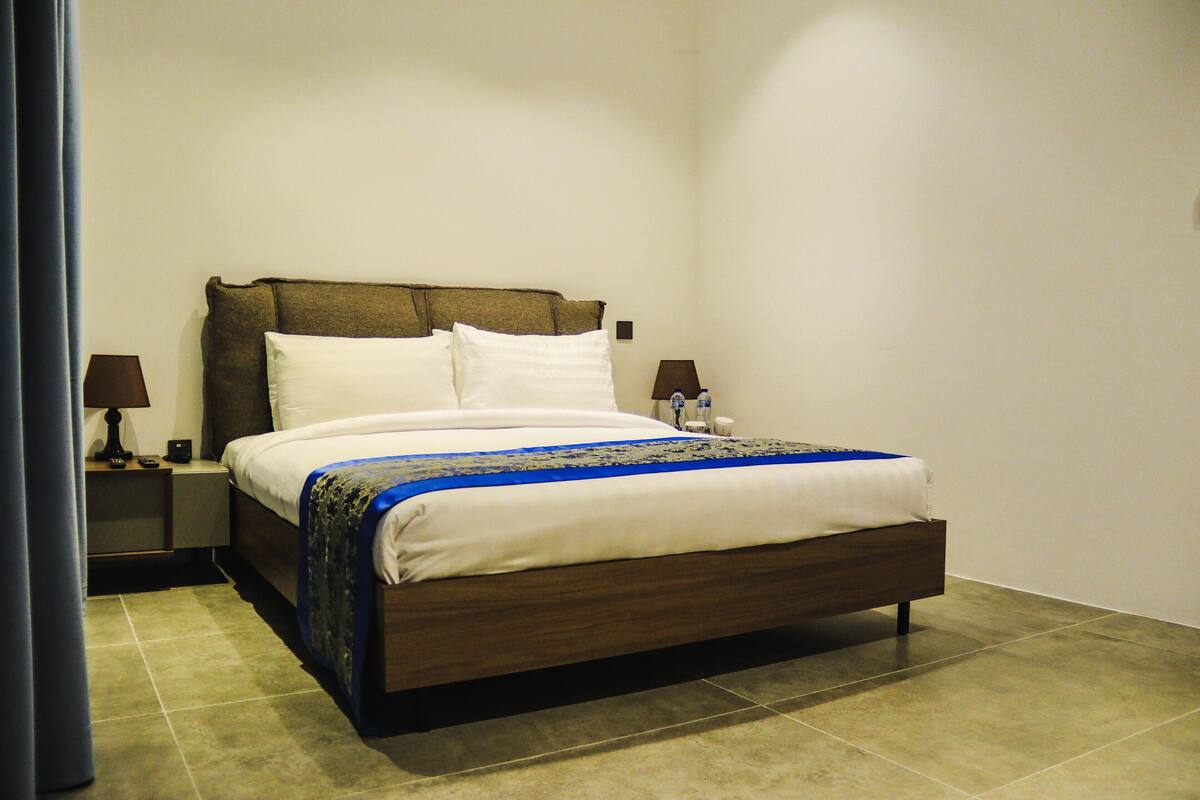 A neatly made bed with a blue and white bedspread, two bedside lamps, and a nightstand with a lamp.