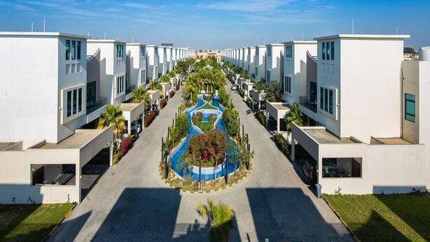 Una zona residencial moderna con edificios blancos uniformes, un área central ajardinada y cielo despejado.