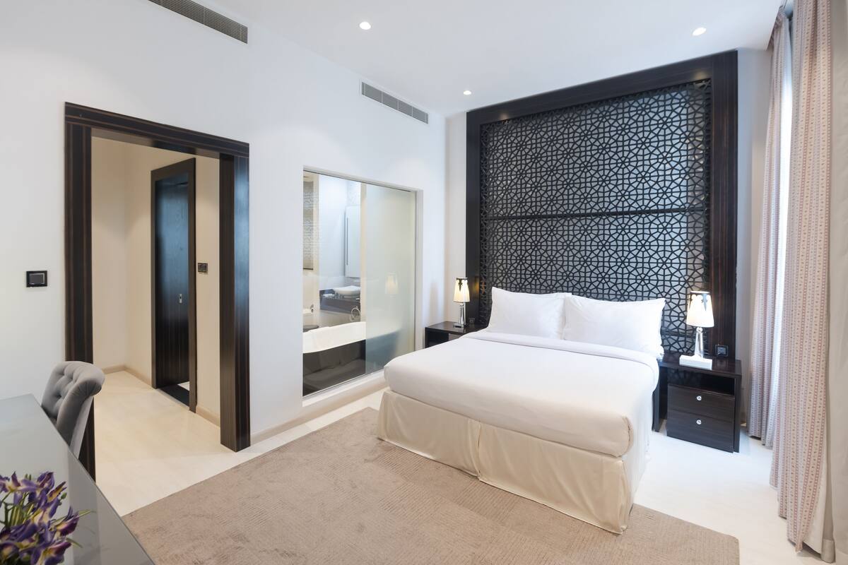 A modern hotel room with a large bed, a nightstand, a mirror, and a view of the bathroom.