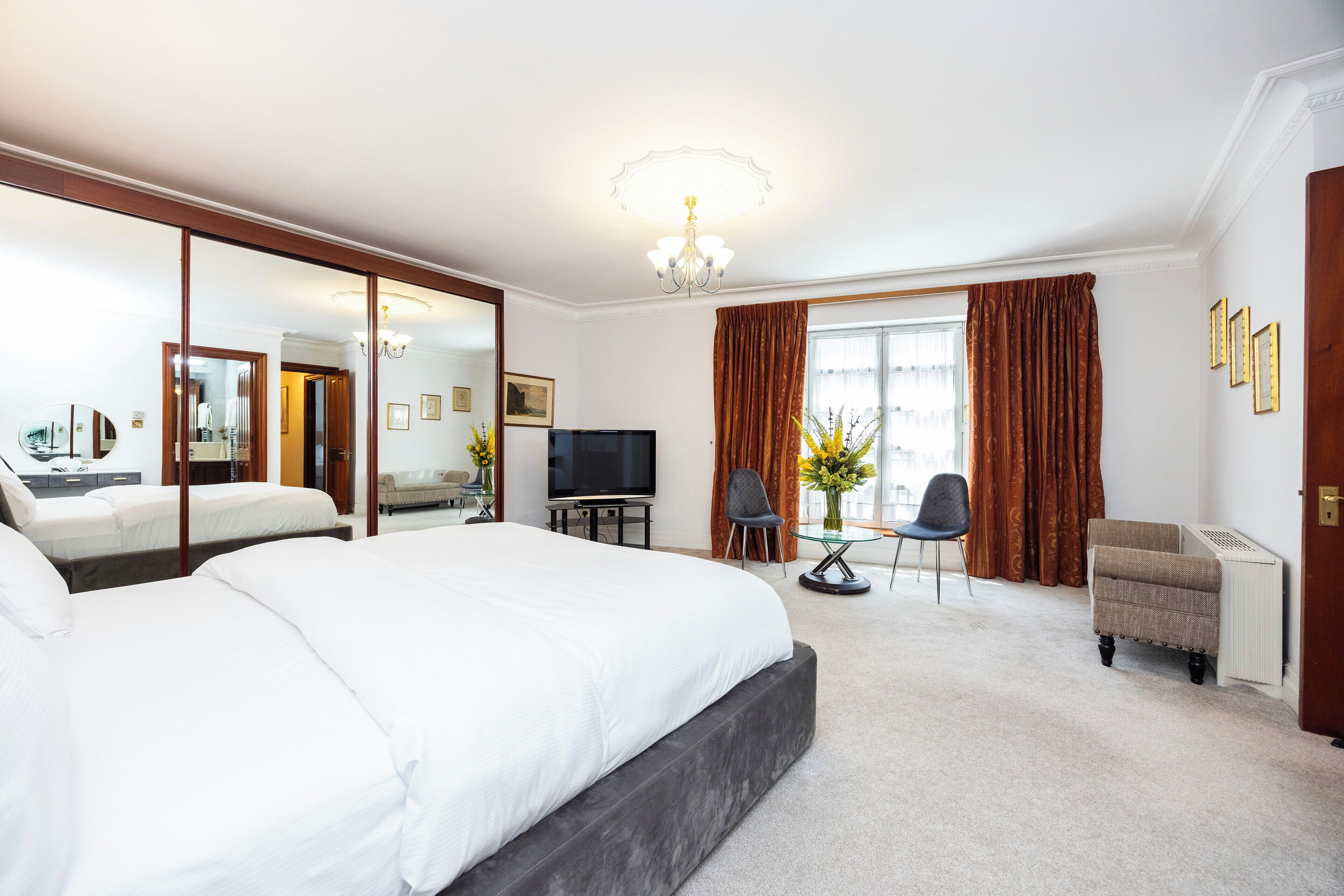 Una habitación de hotel con una cama grande, televisión, escritorio con silla y ventana con cortinas.