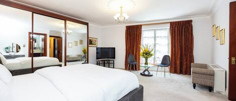 Una habitación de hotel con una cama grande, televisión, escritorio con silla y ventana con cortinas.