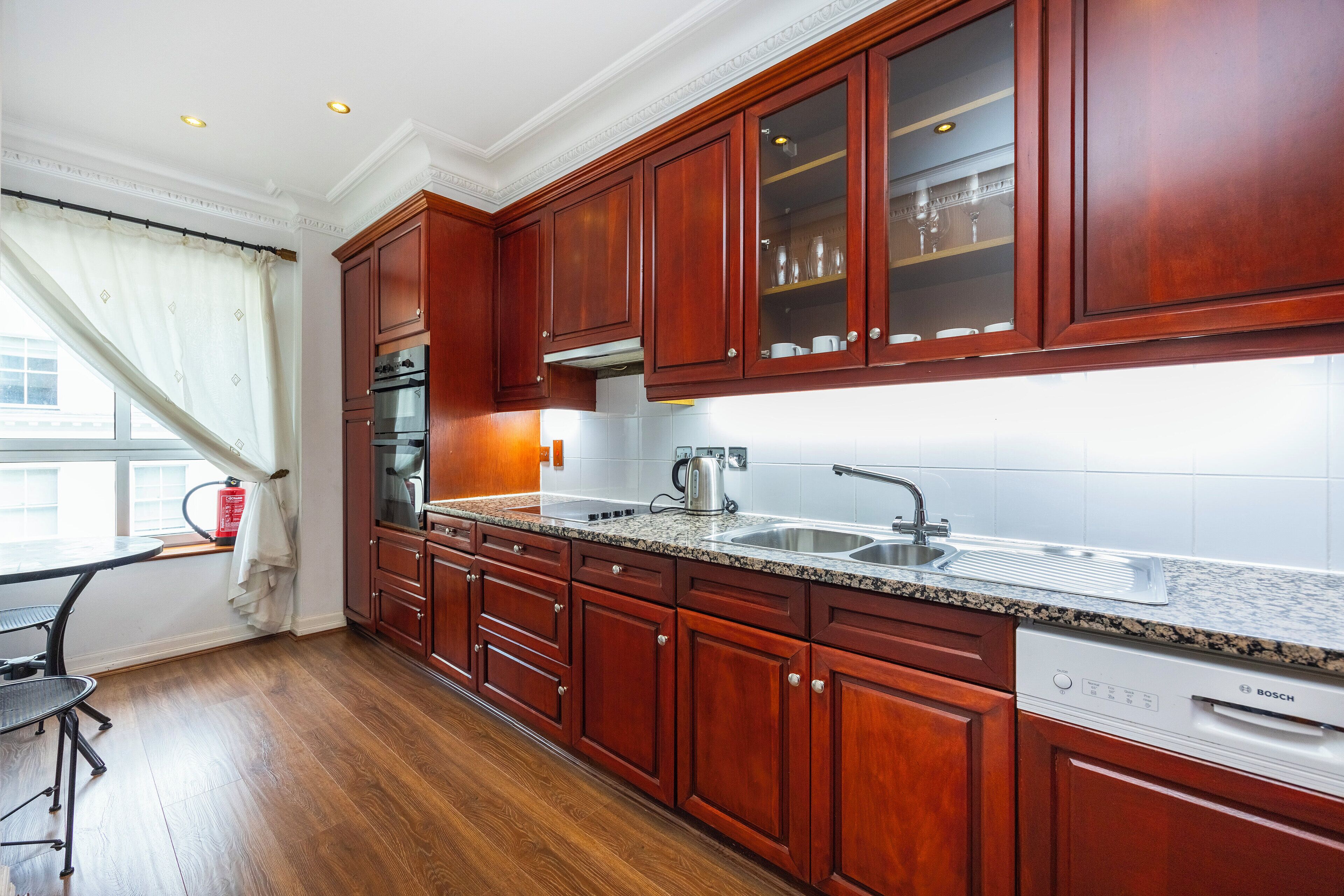 A kitchen with wooden cabinets, a Bosch dishwasher, and a window with curtains.