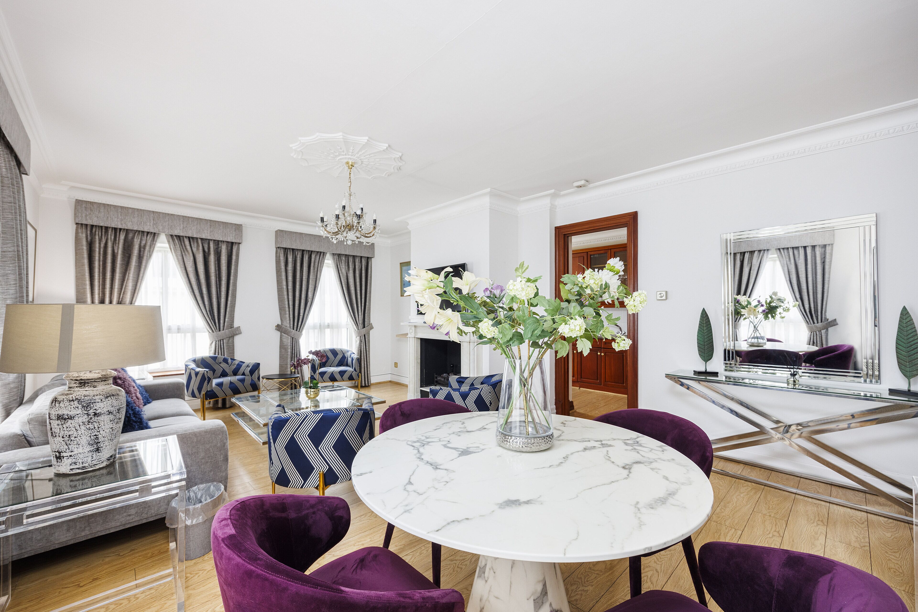 Ein modernes Wohnzimmer mit einem runden Marmortisch, violetten Sesseln, einer Couch und einer Pendelleuchte.