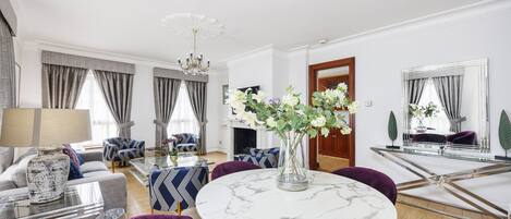 Ein modernes Wohnzimmer mit einem runden Marmortisch, violetten Sesseln, einer Couch und einer Pendelleuchte.