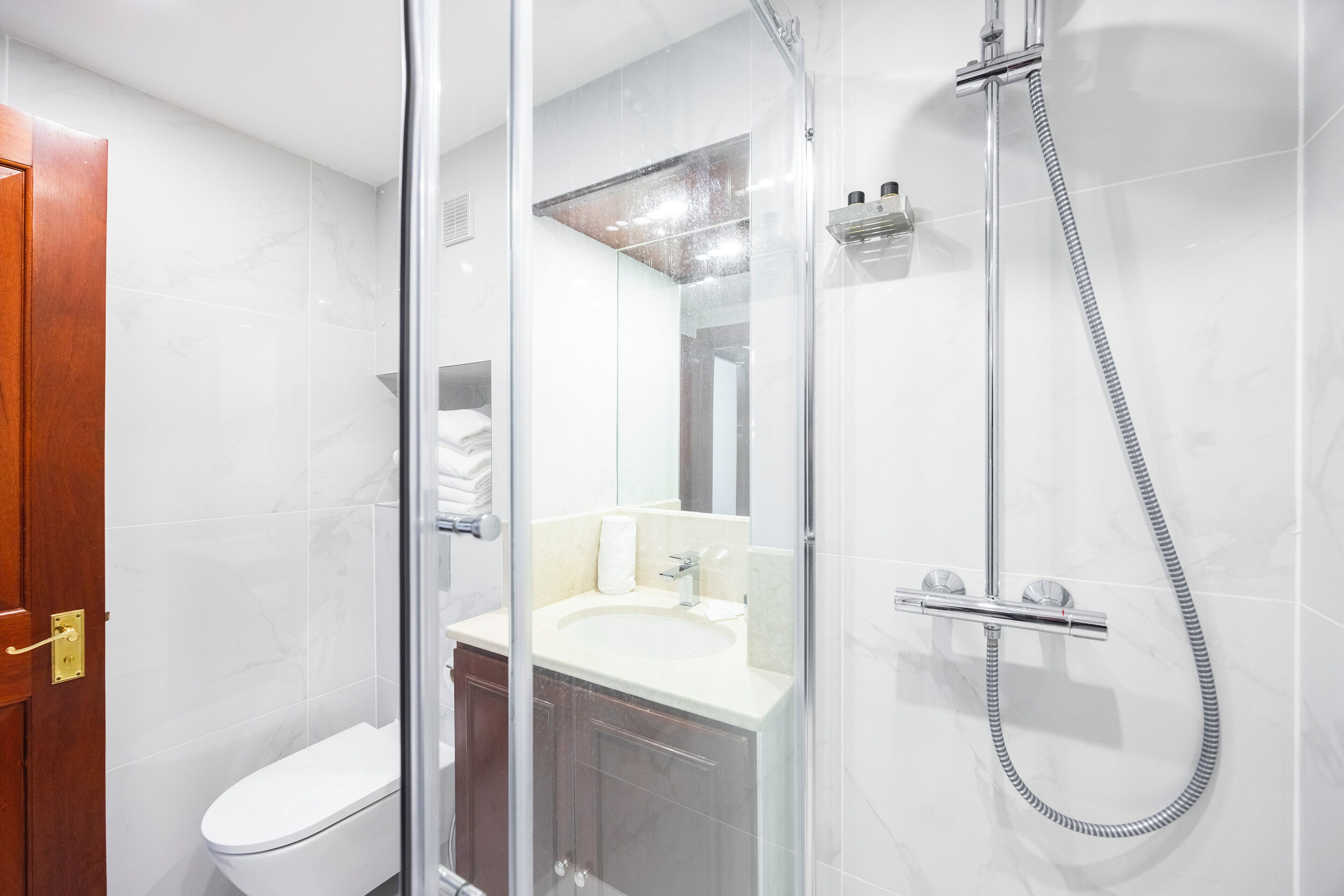 Un baño moderno con ducha envuelta en vidrio, lavamanos blanco y puerta de madera.