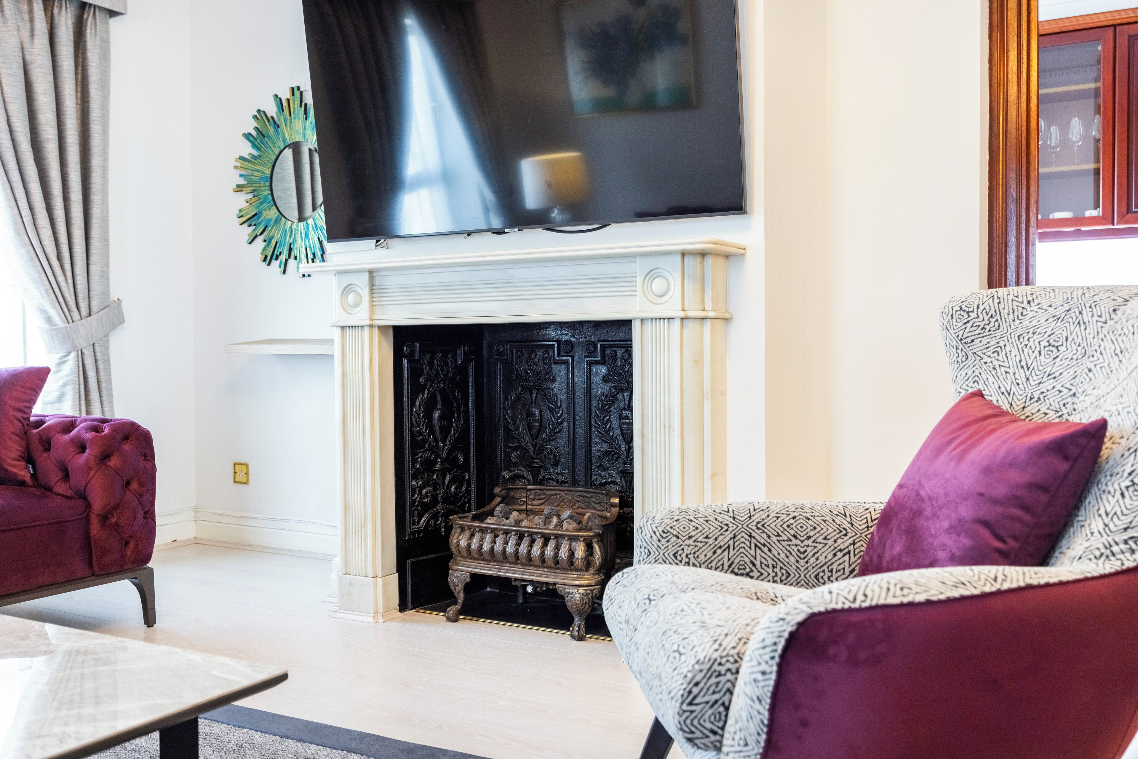 A living room with a fireplace, a television, and two patterned armchairs.
