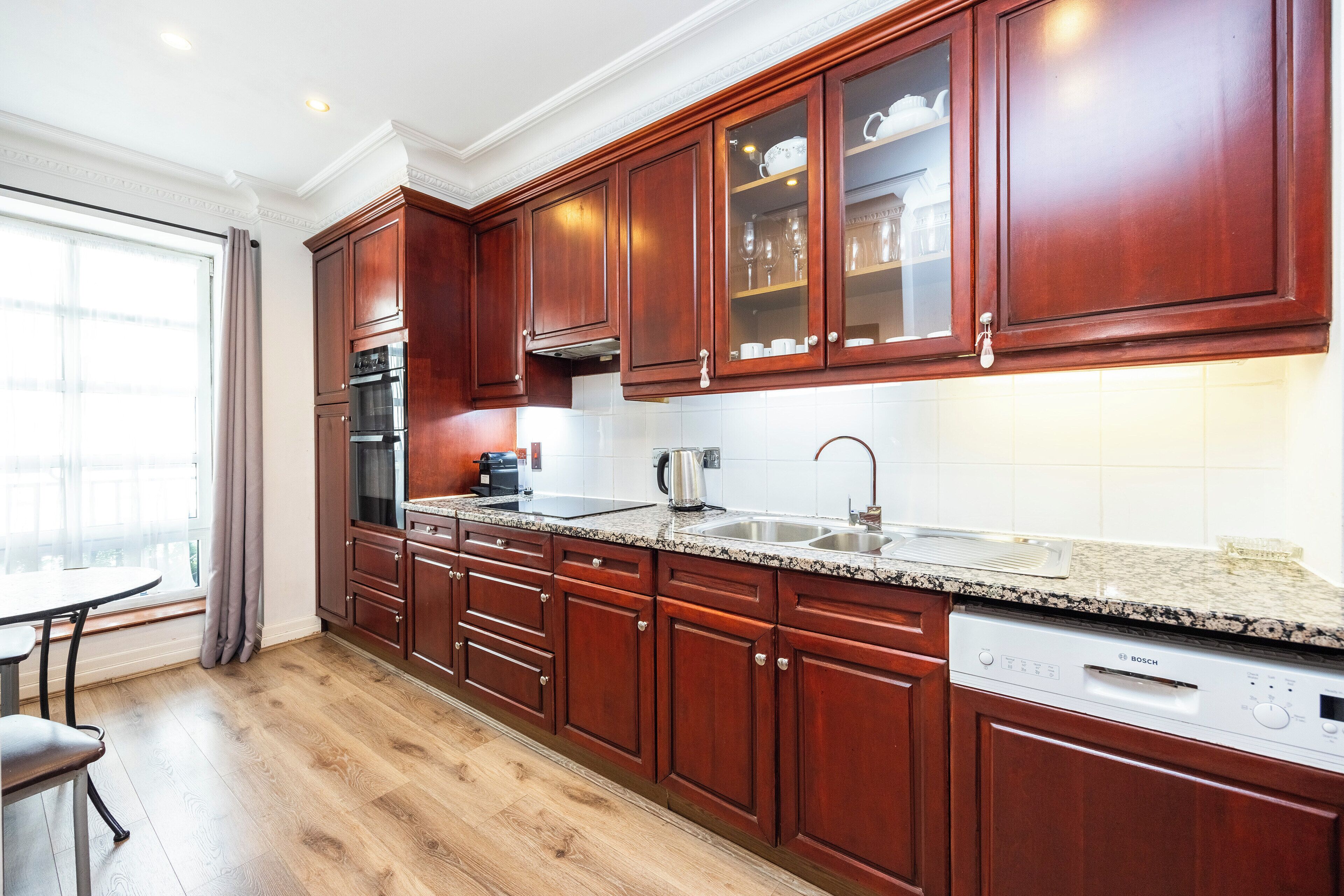 A modern kitchen with wooden cabinets, a Bosch dishwasher, and a large window with curtains.