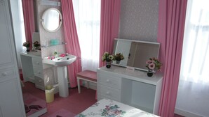 Une chambre à coucher aux couleurs rose et blanc, avec un miroir rond, une table de chevet et une couvre-lit à motifs floraux.