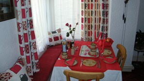 Un coin repas avec une nappe rouge, un vase contenant une seule fleur et une horloge au mur.