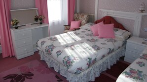 Une chambre à coucher avec une couvre-lit à motifs floraux, une table de chevet, une commode et une chaise.