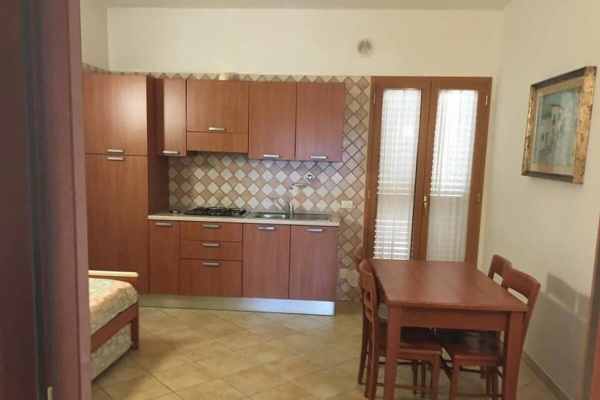 Cocina compacta con armarios de madera, una mesa de comedor con sillas y piso de baldosas.
