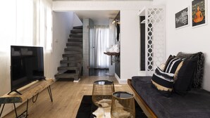 A modern living room with a flat-screen TV, a sofa, and a staircase leading to an upper level. - Suite Azur Hotel (Essaouira)