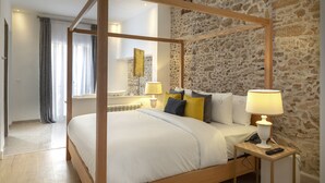 A four-poster bed with a wooden frame, a bedside table with a lamp, and a stone wall in the background. - Suite Azur Hotel (Essaouira)