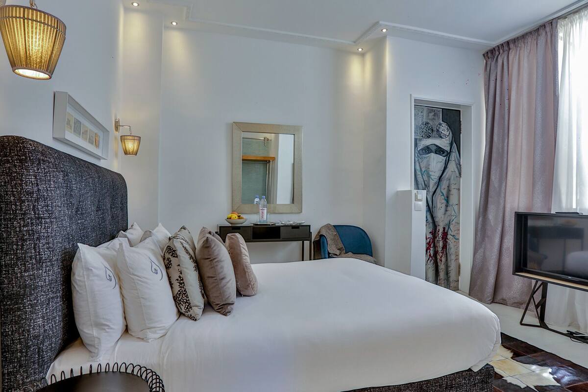 Habitación de hotel con una cama grande, un escritorio, una silla, un televisor y un espejo.