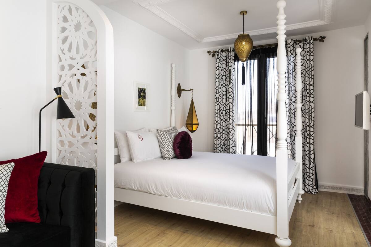 Una cama con dosel con ropa de cama blanca, una lámpara de pie negra y cortinas estampadas.