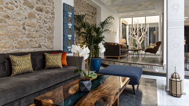 A modern living room with a stone wall, a blue potted plant, a grey sofa, and a wooden coffee table. - Suite Azur Hotel (Essaouira)