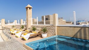 A rooftop pool area with lounge chairs, a small pool, and a stone wall. - Suite Azur Hotel (Essaouira)