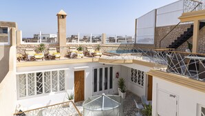 A rooftop terrace with sun loungers, a glass table, and a pool. - Suite Azur Hotel (Essaouira)