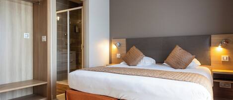 A modern hotel room with a large bed, a walk-in closet, and a bedside table with a lamp.
