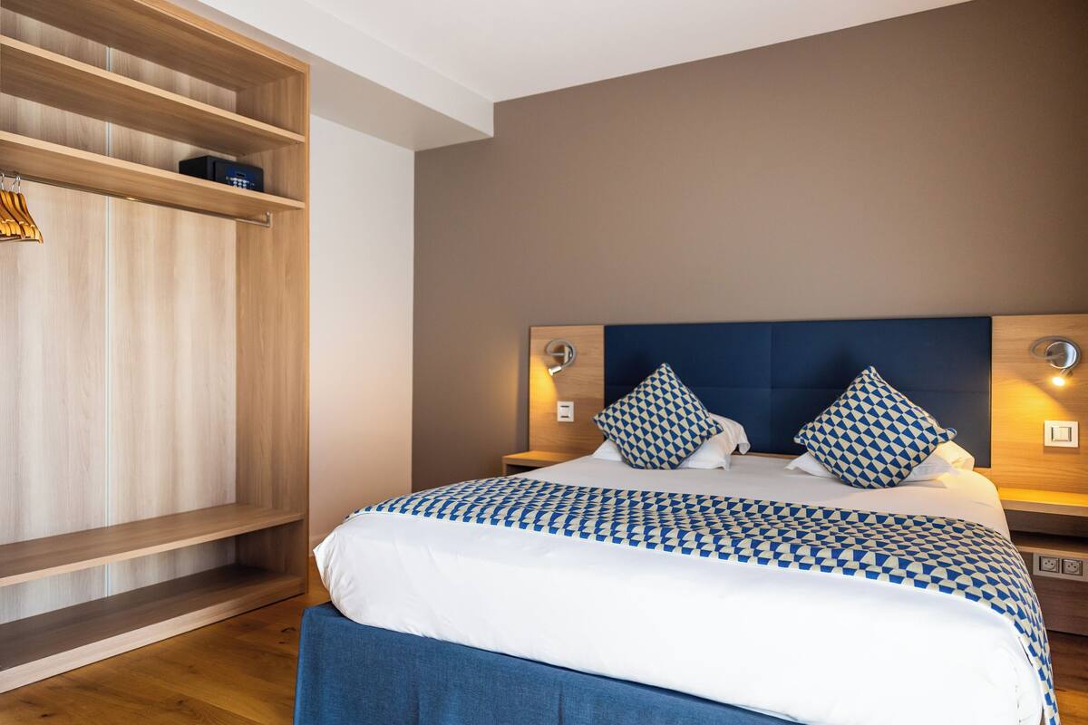 A neatly arranged hotel room with a large bed, wooden shelving, and a modern headboard.