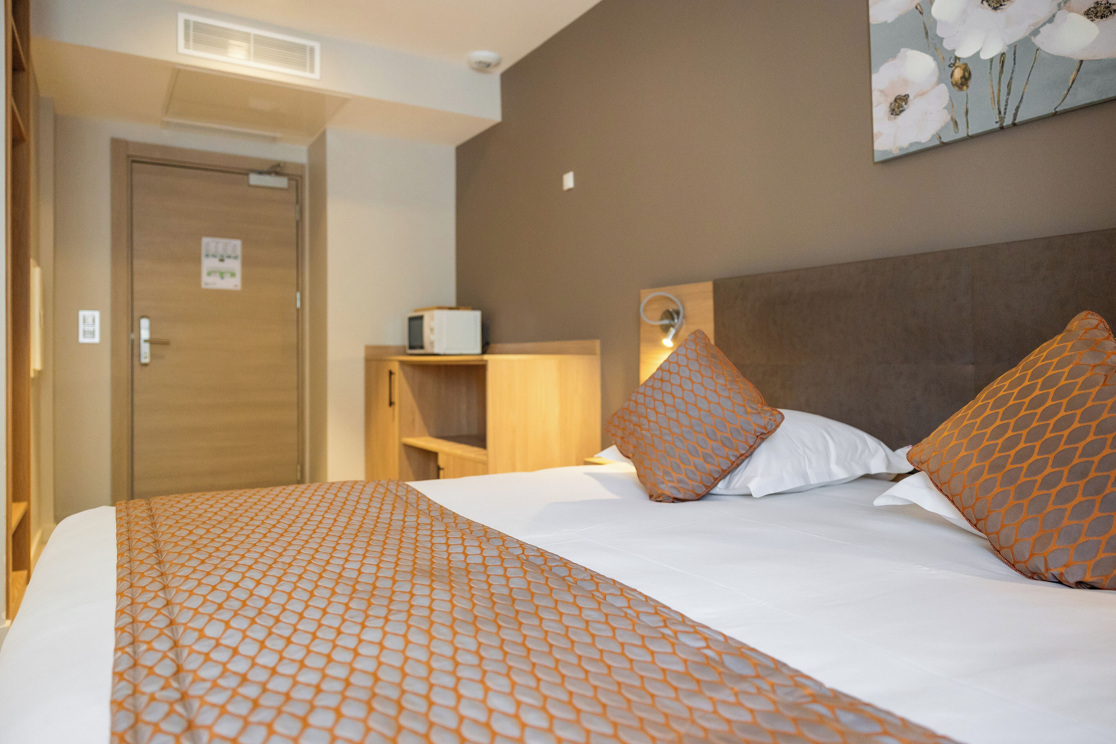 Una habitación de hotel con una cama bien hecha, un armario de madera y una estantería en la pared.