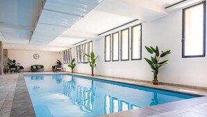 An indoor swimming pool with clear blue water, surrounded by tiled flooring and potted plants. - Hôtel Le Bastia (Bastia)