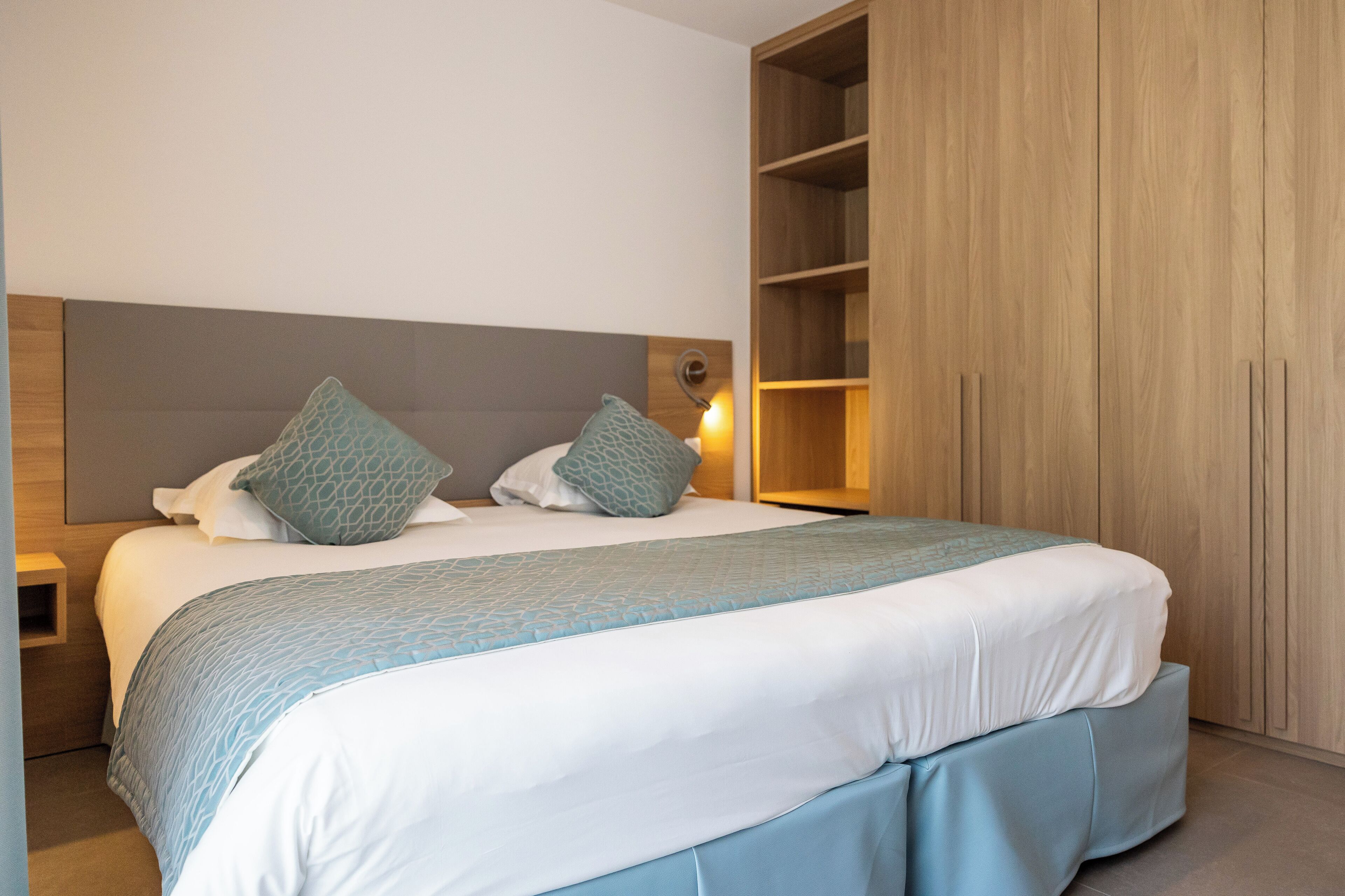A neatly made bed with a grey headboard, two pillows, and a blue bedspread.