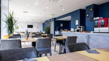 Een moderne eetruimte met tafels en stoelen, een bar met een koffieapparaat en een grote potplant.