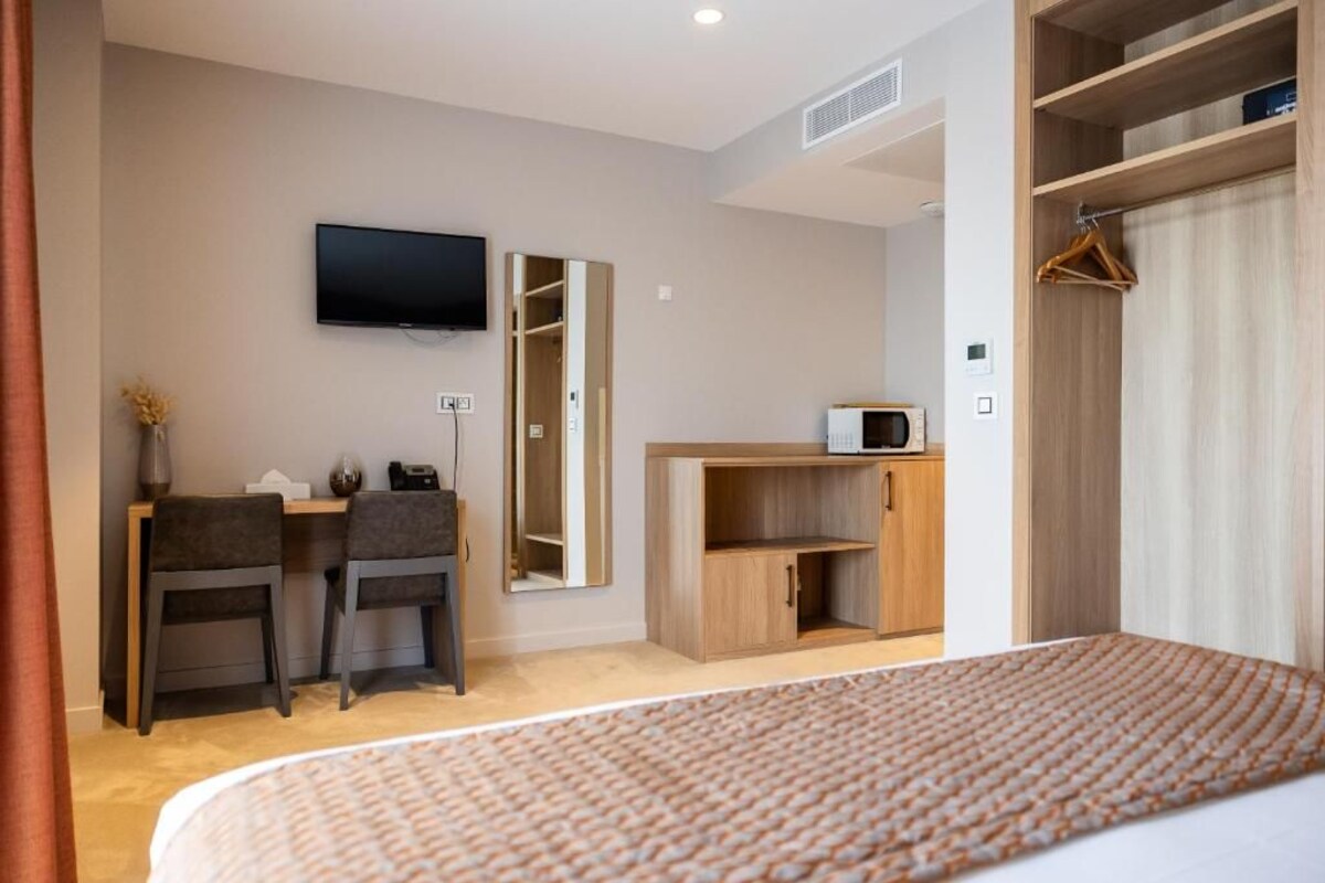 Habitación de hotel con cama, escritorio con dos sillas, televisión montada en la pared, armario y un mueble pequeño.