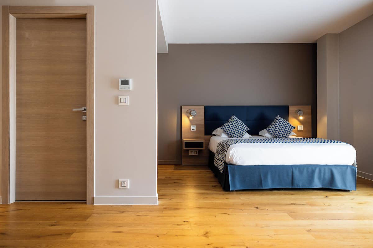 A bedroom with a wooden floor, a bed with a blue and white bedspread, two bedside tables with lamps, and a wooden headboard.