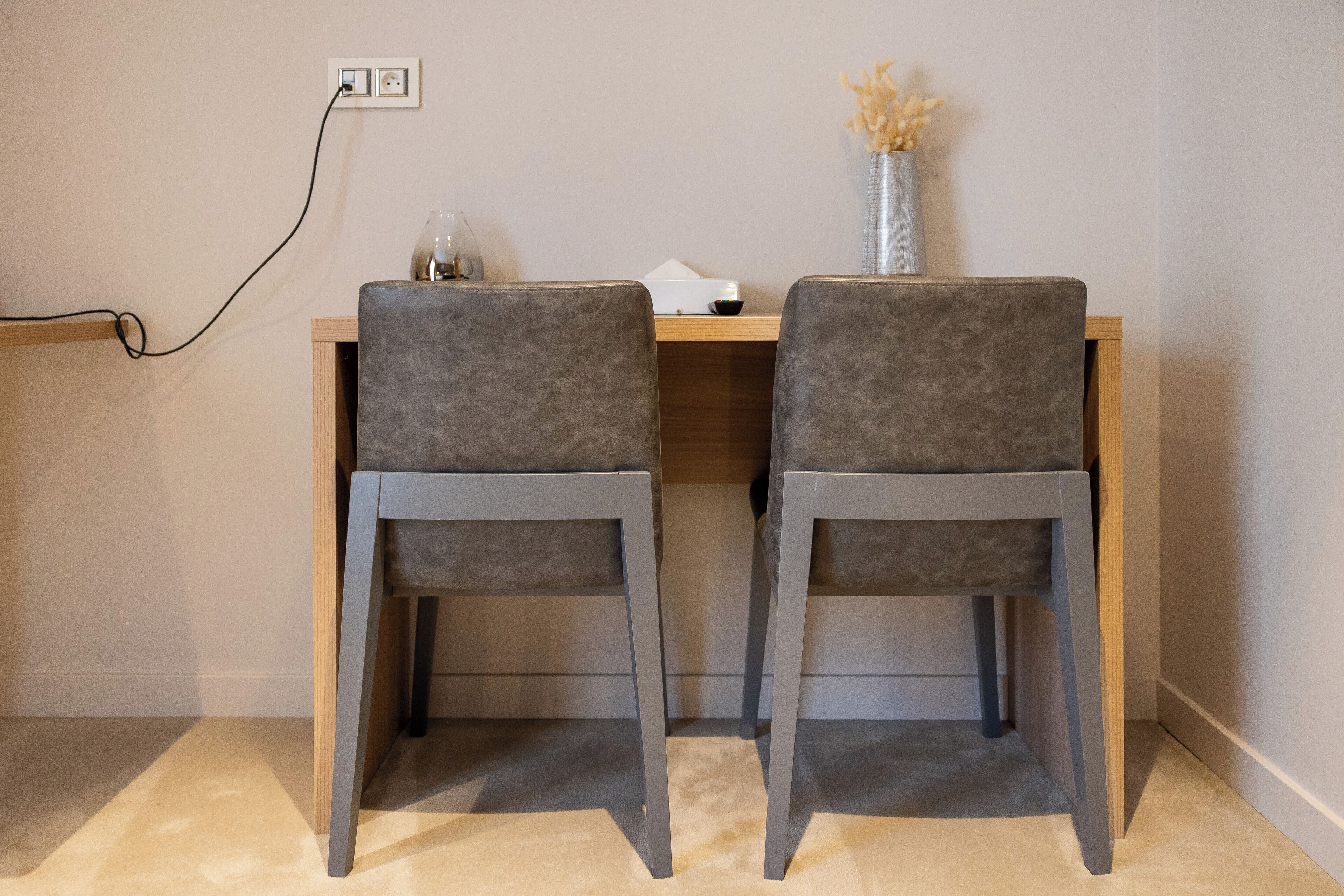 Un bureau avec deux chaises grises, un vase contenant des fleurs séchées et une lampe.