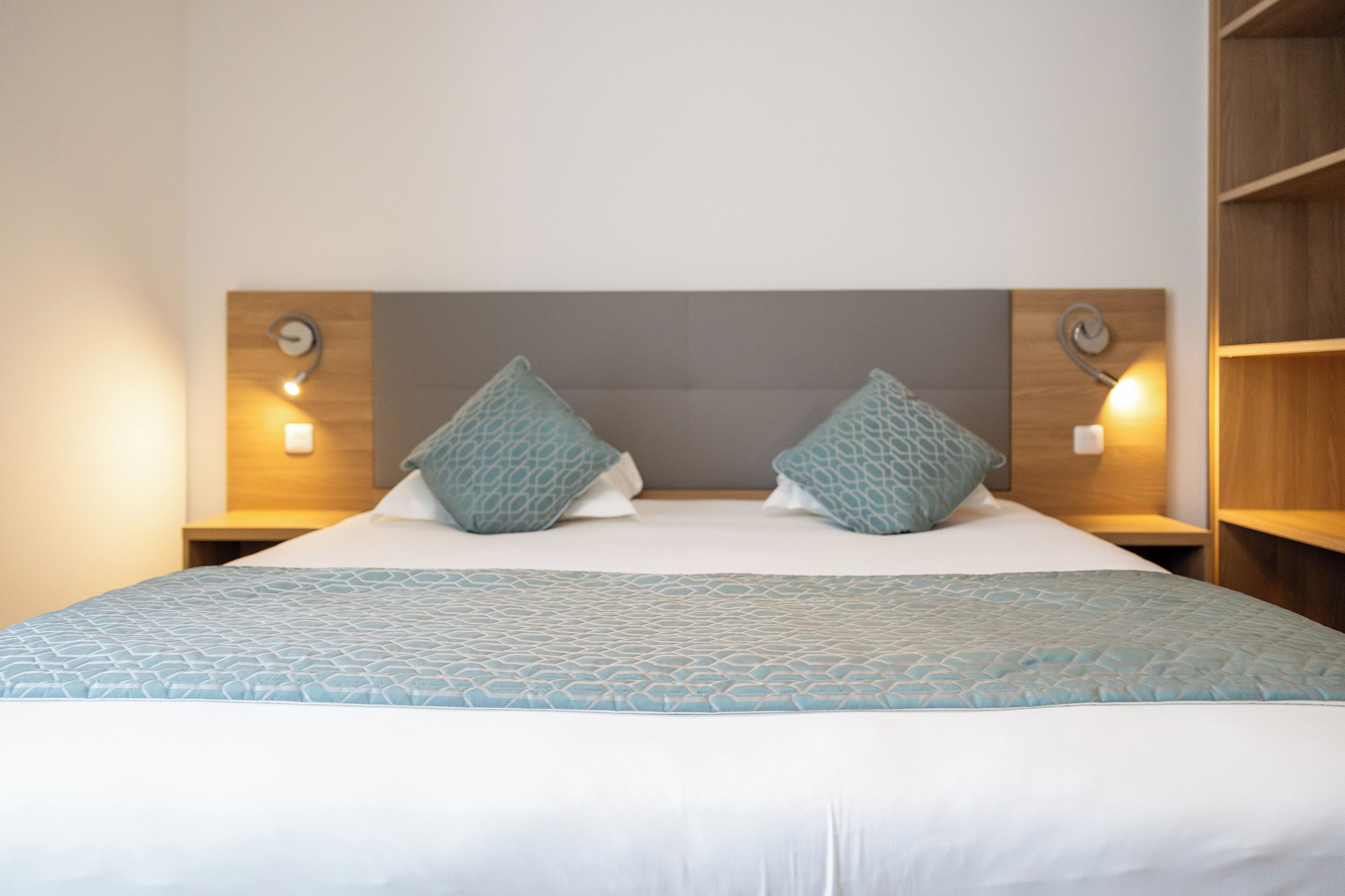A neatly made bed with a patterned bedspread and pillows, flanked by two bedside tables with wall-mounted lamps.