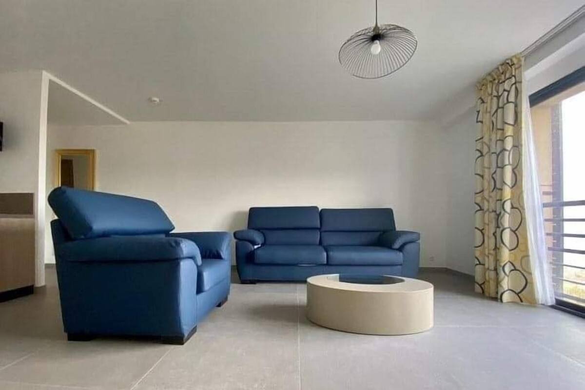 A modern living room with two blue sofas, a round coffee table, and a pendant light.