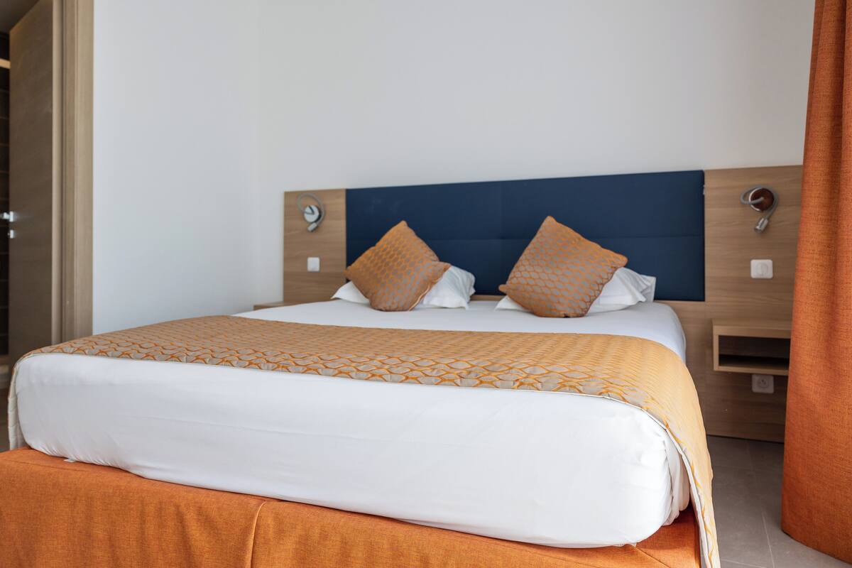 A neatly made bed with a patterned bedspread and two pillows, a wooden headboard, and a bedside table with a lamp.