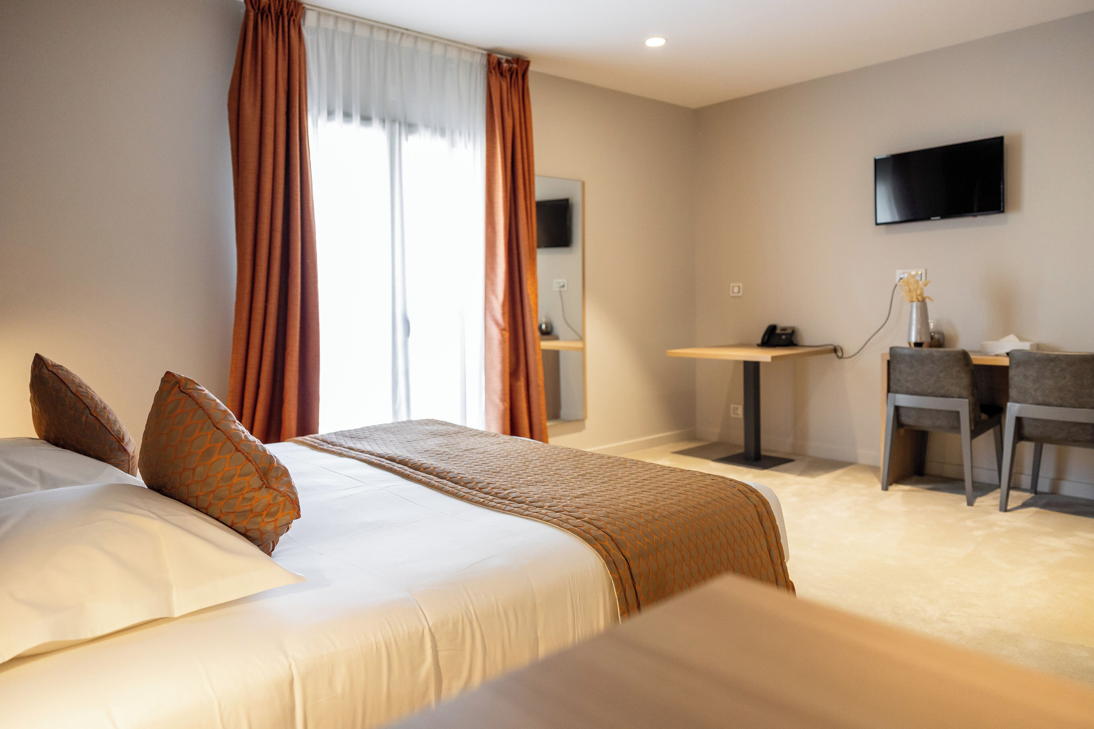 Een hotelkamer met een bed, een bureau, een stoel, een televisie en een raam met gordijnen.