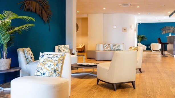 A modern hotel lobby with white sofas, a large potted plant, and a curved seating area. - Hôtel Le Bastia (Bastia)