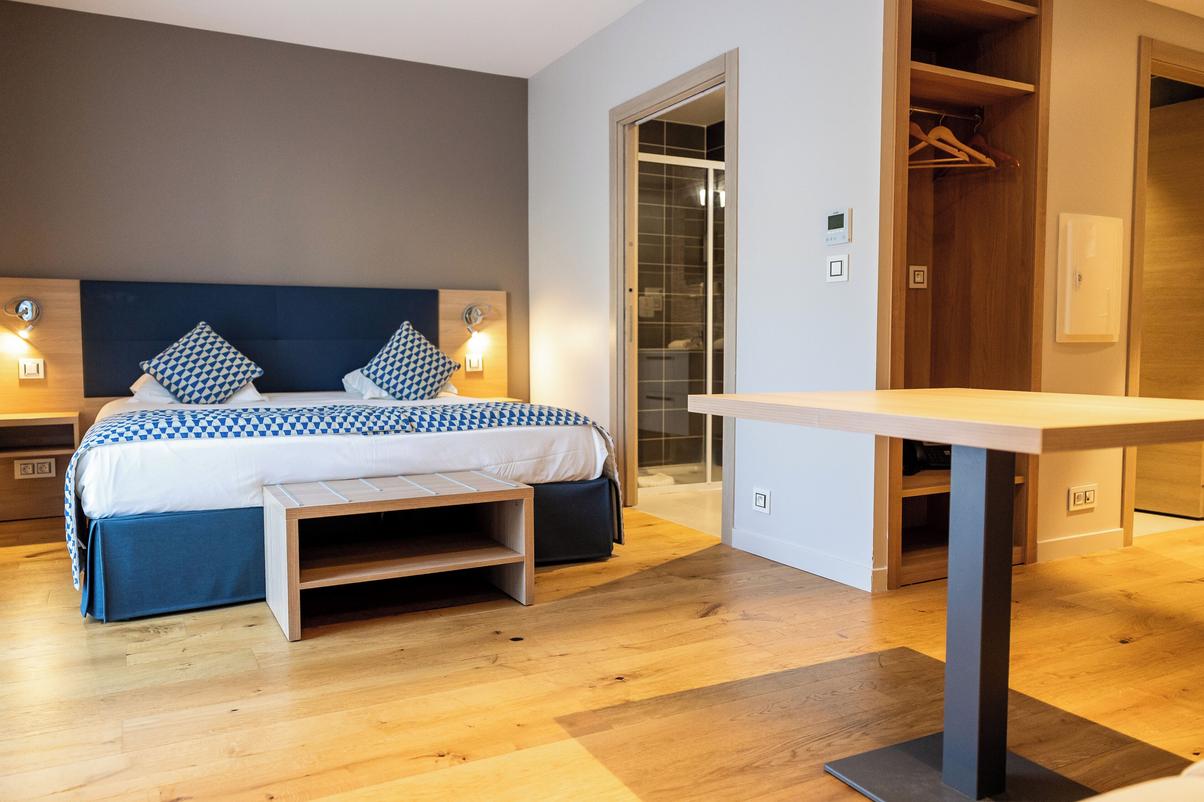 Un dormitorio moderno con cama, mesitas de noche, un banco y una mesa.