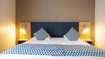 Una cama bien hecha con colcha y almohadas a cuadros, flanqueada por dos mesitas de noche con lámparas.