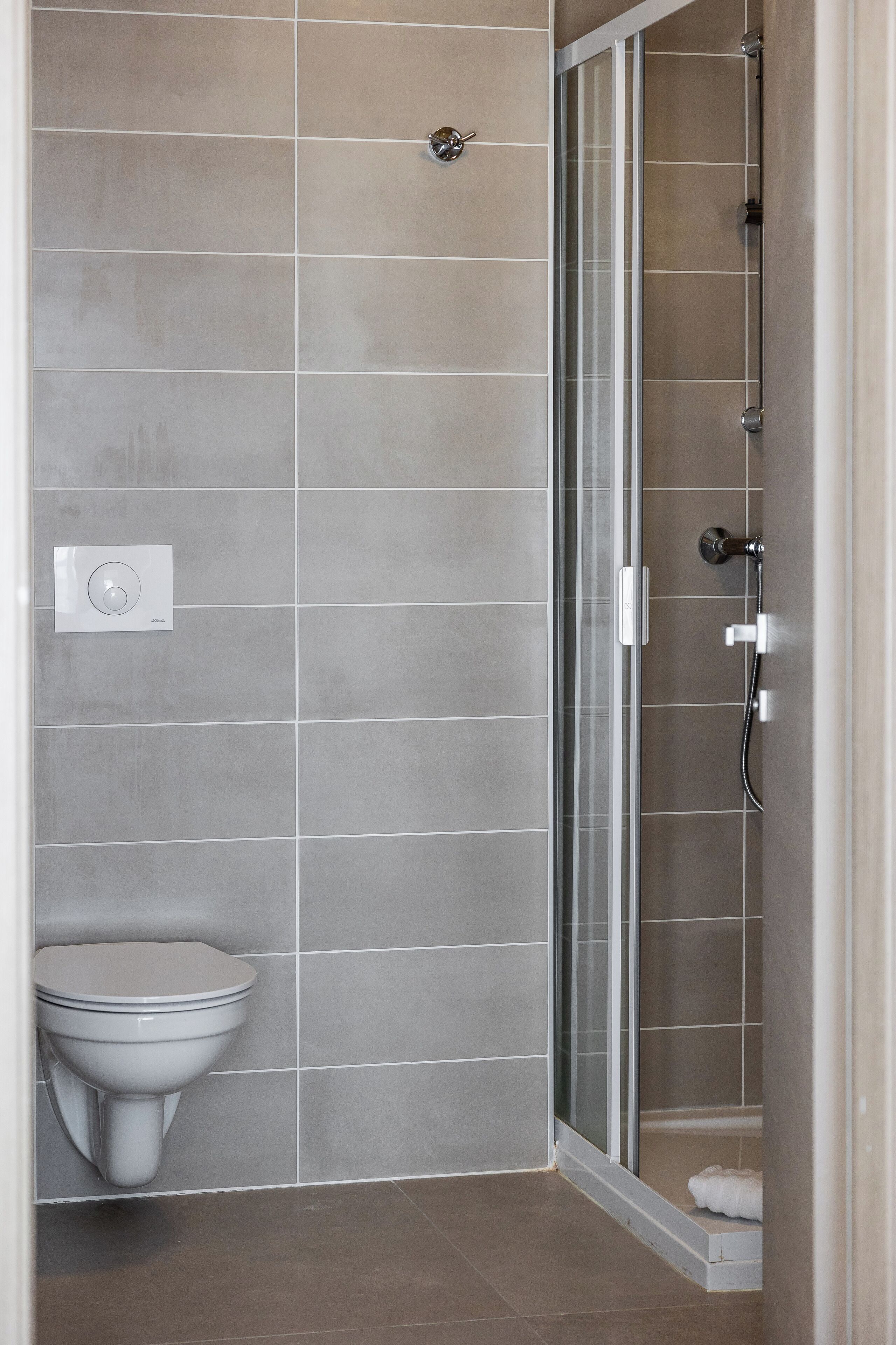 Een moderne badkamer met toilet, douche met glazen deur en bedieningspaneel aan de muur.