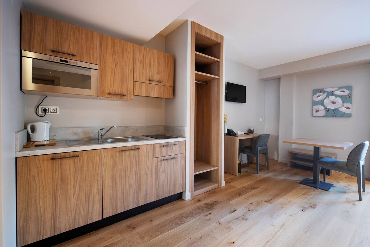 A modern kitchen with wooden cabinets, a built-in oven, and a dining area with a table and chairs.