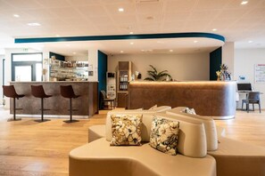 Zona de recepción de un hotel con mostrador curvo, bar y área de descanso.
