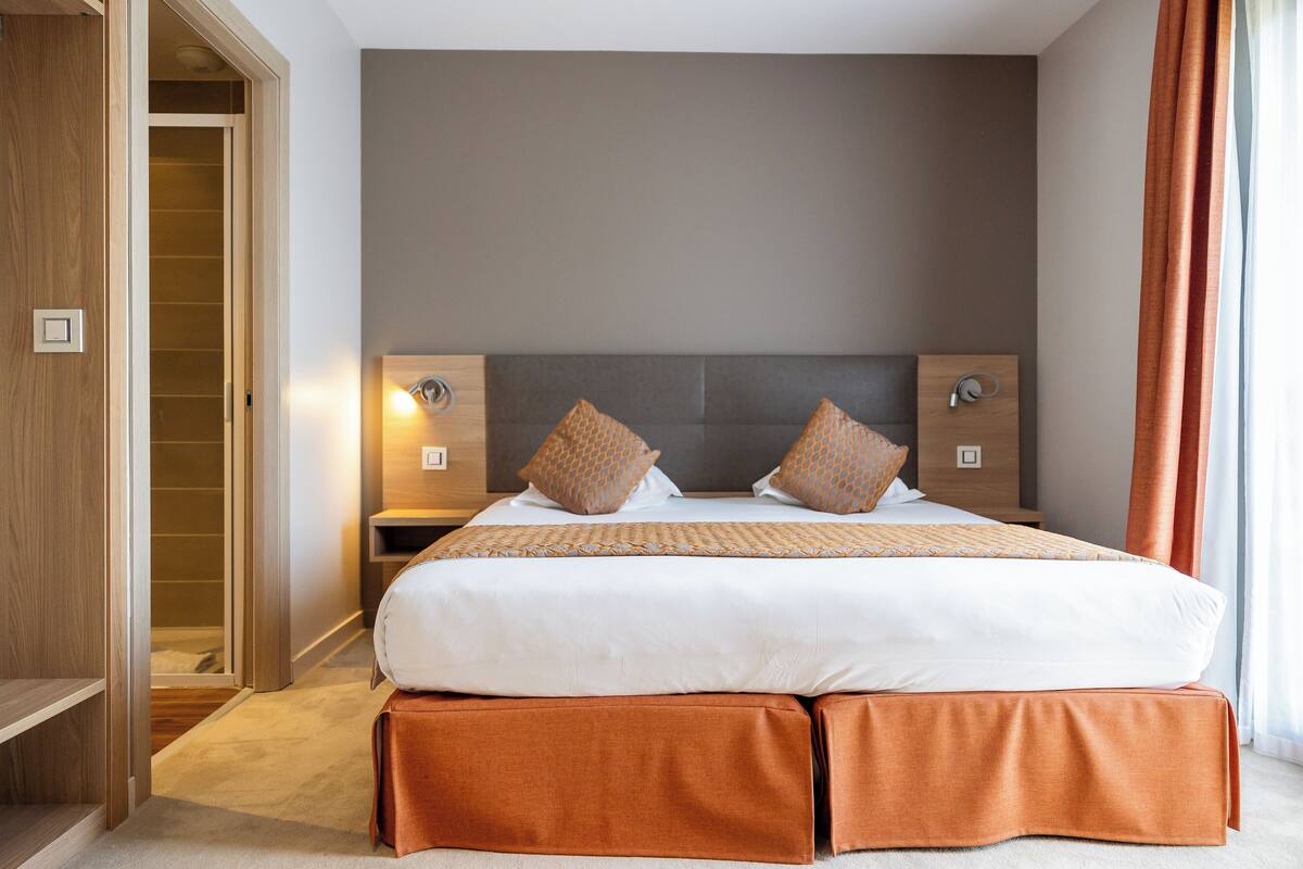 A bedroom with a large bed, two bedside tables, a wardrobe, and a door to a bathroom.